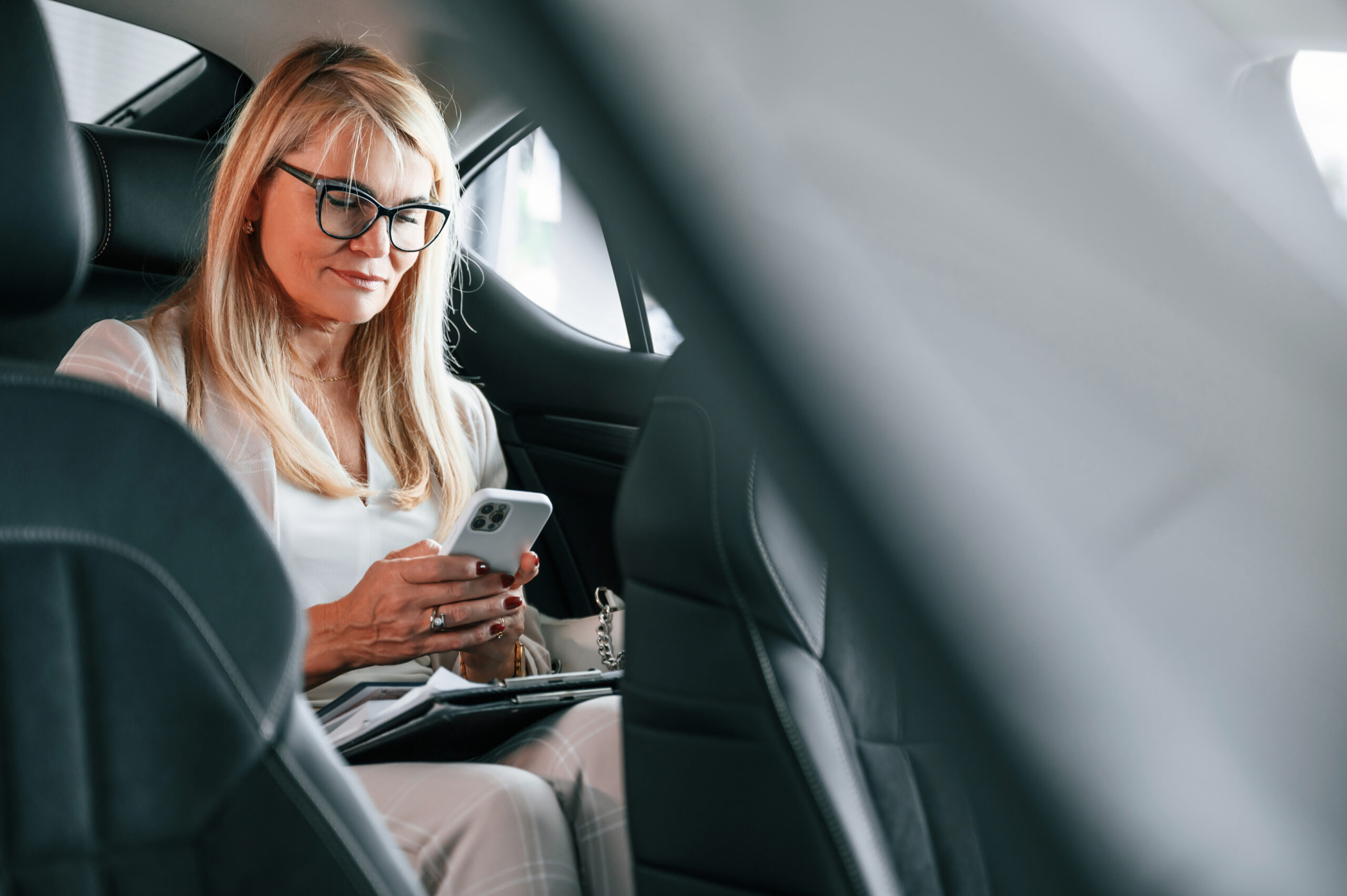 Sitting on the backseat and working. Woman in white formal clothes is in the car dealership